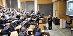 ミュー粒子を利用した東京電力福島第一原発１号機の建屋内部の調査について説明する高﨑名誉教授（右）＝２０日、茨城大日立キャンパス