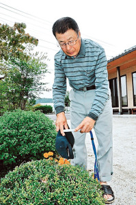 自宅の植え込みに線量計をかざす久保田さん。村民の帰還を促すためには再除染が必要だと感じている