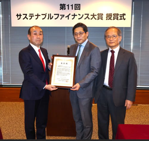 サステナブルファイナンス大賞の受賞式で、審査員の1人待場智雄氏より表彰状を受け取る小宮氏㊧。㊨は環境金融研究機構の藤井良広