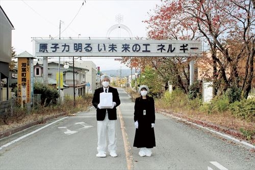 防護服と喪服を着込んだ大沼さん夫妻。納骨で福島県双葉町を訪れた際、セルフタイマーで撮影した＝２０１３年１１月９日