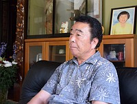 渡辺はま子さんの遺影（右上）が置かれた部屋で取材に応じる夫の幹夫さん＝７月２８日、福島県川俣町