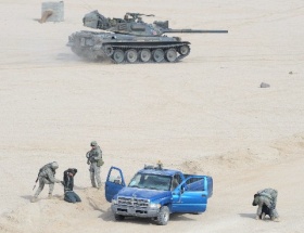 不審者役の俳優を尋問する米兵の横を通過する陸上自衛隊の７４式戦車＝昨年１月、米カリフォルニア州の米陸軍戦闘訓練センター（菊池雅之氏提供）