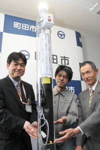 透明の管に付けた新たな蓄電装置を紹介する開発メンバー＝東京・町田市役所で