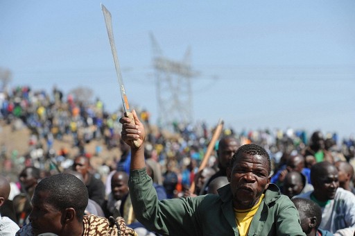 南アフリカ・マリカナ（Marikana）の鉱山で、なたを振り上げる座り込みに参加したストライキ中の労働者（2012年8月16日撮影）。 ©AFP＝時事